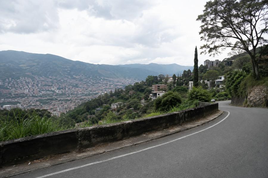 A curving hillside road high above the Aburrá Valley, houses stepping down the slope.