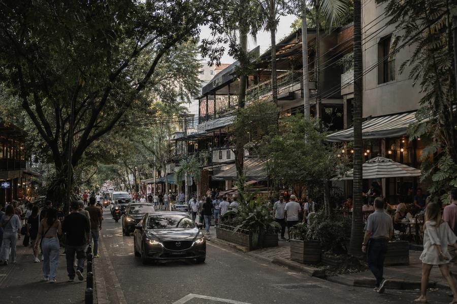 A dense commercial street at dusk with cafés, awnings and heavy foot traffic.